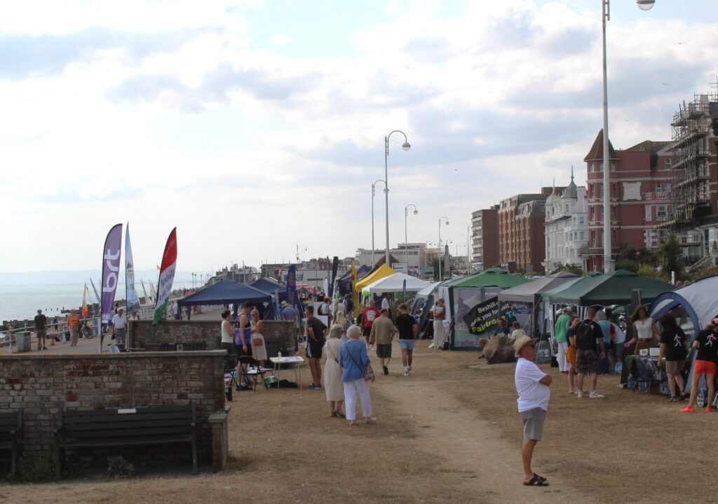 A wide shot of the stalls and flags making up the Bexhill Day exhibits along East Parade seafront.